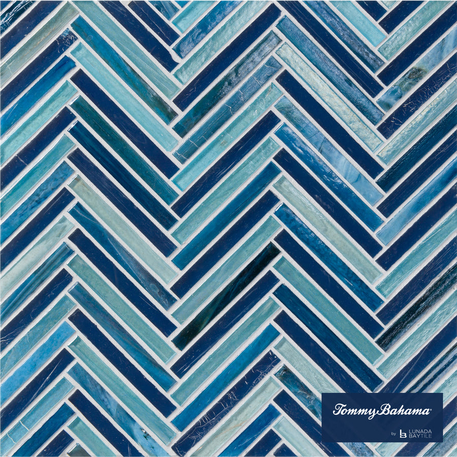 The Tommy Bahama Zig & Zag Mosaic Tile in Lucky Bay Mix features a glossy herringbone pattern of rectangular blue, teal, and white tiles with varying shades. The Tommy Bahama by Lunada Bay Tile logo is in the bottom right corner.