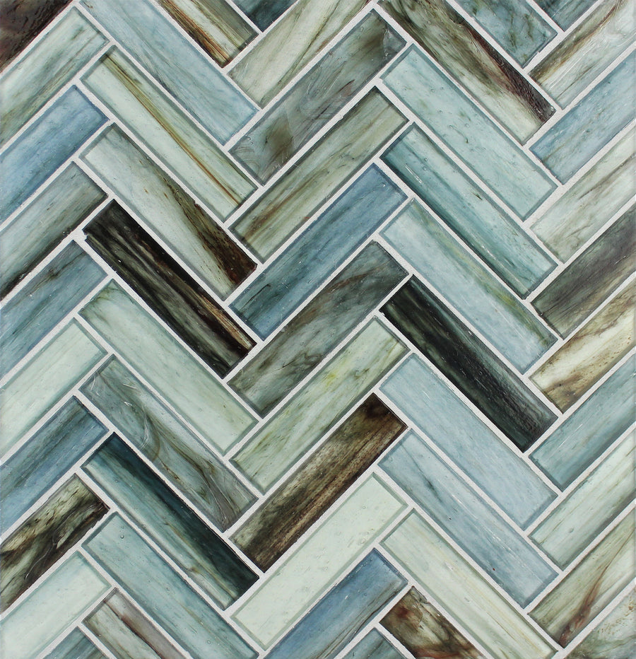 The Tozen Herringbone Mosaic Tile in Natural features a pattern of rectangular tiles in green, blue, and gray shades, separated by white grout lines.