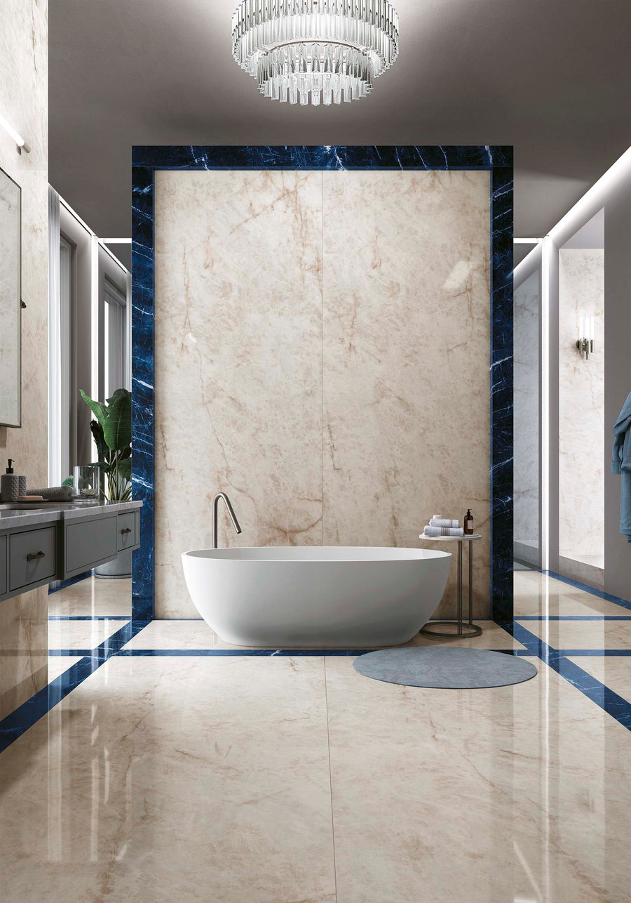Luxurious modern bathroom with a freestanding white bathtub, marble floors and walls, blue marble trim, glass chandeliers, floating vanities, and a circular gray bath mat. The space is spacious, elegant, and well-lit.