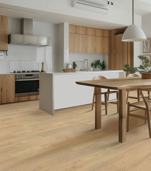 Modern kitchen and dining area with light wood floors, wooden cabinets, white countertops, a dining table with chairs, pendant light, houseplants, and stainless steel appliances. The space feels bright and minimalist.