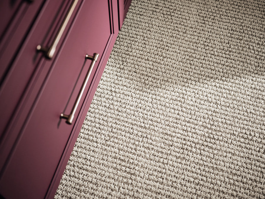 Close-up of textured beige carpet next to purple cabinets with silver handles. The image is taken at an angle, showing a portion of both the carpet and the cabinetry.