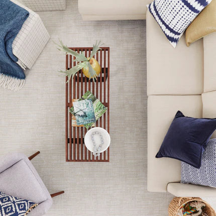 A top-down view of a modern living room with a beige sectional sofa, blue and patterned cushions, a wooden slatted coffee table with decor, a gray armchair, and a blue throw blanket.