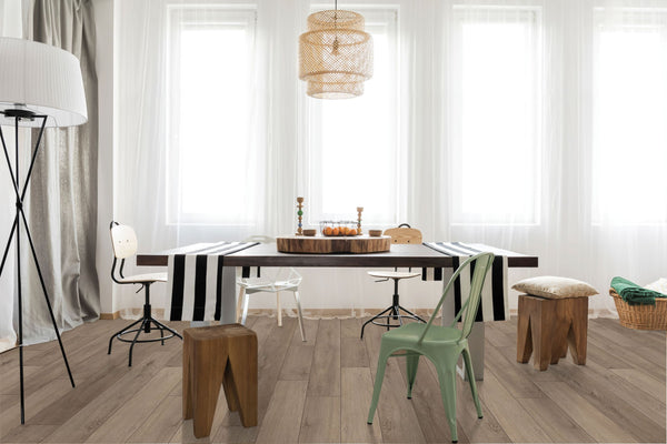 A modern dining room with a wooden table, assorted chairs and stools, striped table runners, decorative candles, a pendant light, tall floor lamp, and large windows with sheer white curtains.