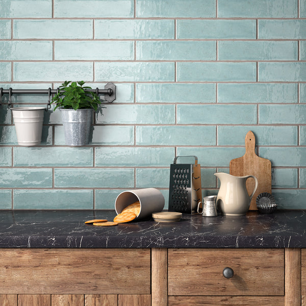 A kitchen countertop with a spilled can of cookies, a cheese grater, ceramic jug, mug, cutting boards, a brush, and potted herbs hanging on a rack against a light blue tile backsplash.