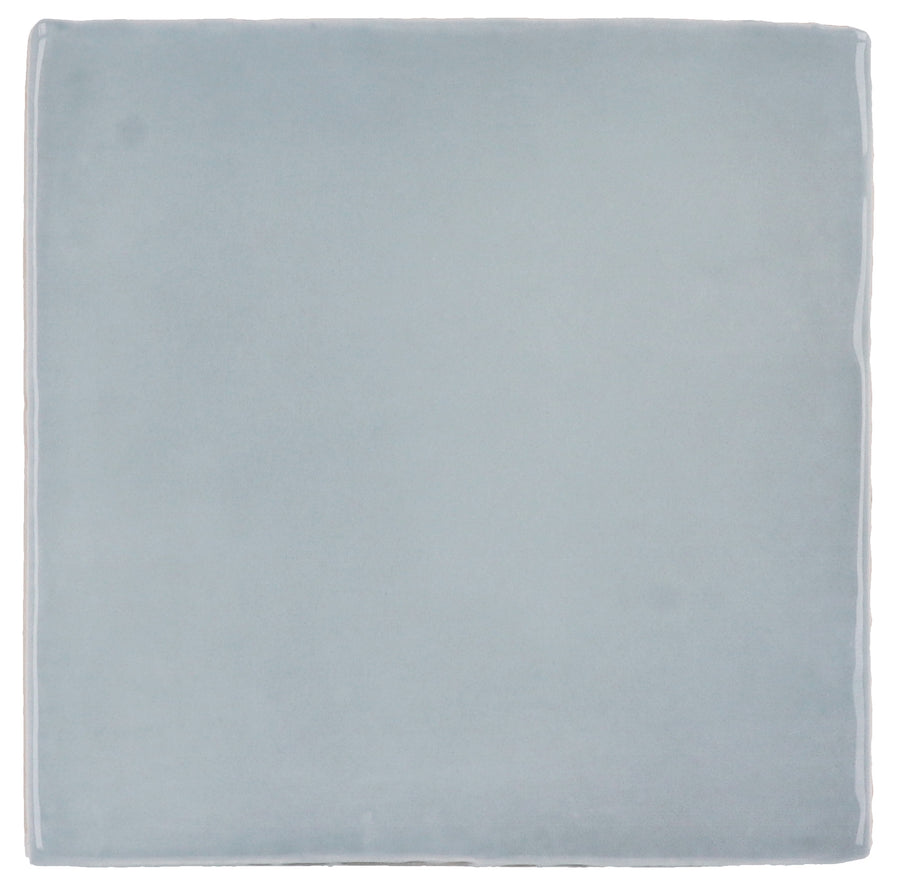 The Manacor 4" x 4" Ceramic Tile in Blue Moon features a smooth surface and slightly rounded edges, evoking Spanish elegance. Displayed against a white background, its soft blue tone adds a refined touch to any space.
