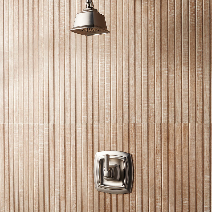 A modern shower with a square metal showerhead and matching square control handle, mounted on a wall with vertical, textured beige tiles.
