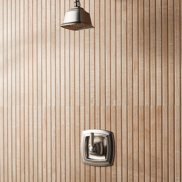 A modern shower with a square metal showerhead and matching square control handle, mounted on a wall with vertical, textured beige tiles.