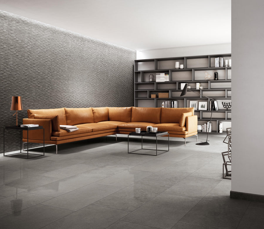 Modern living room with a large orange sectional sofa, black metal coffee tables, textured gray wall, built-in shelves with books and decor, and gray tile flooring. Warm lighting adds a cozy atmosphere.