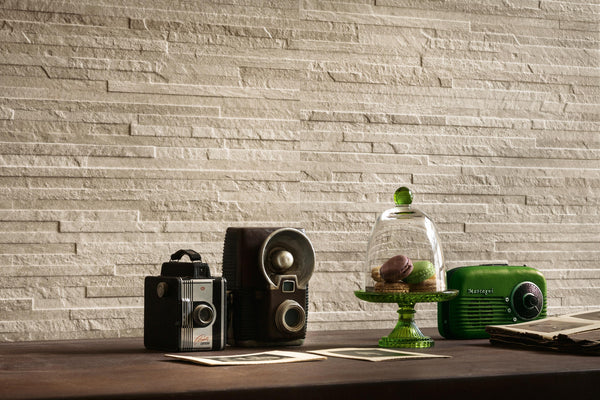 A table with two vintage cameras, old photos, a green glass stand with macarons under a dome, and a green retro radio, set against a textured beige stone wall.