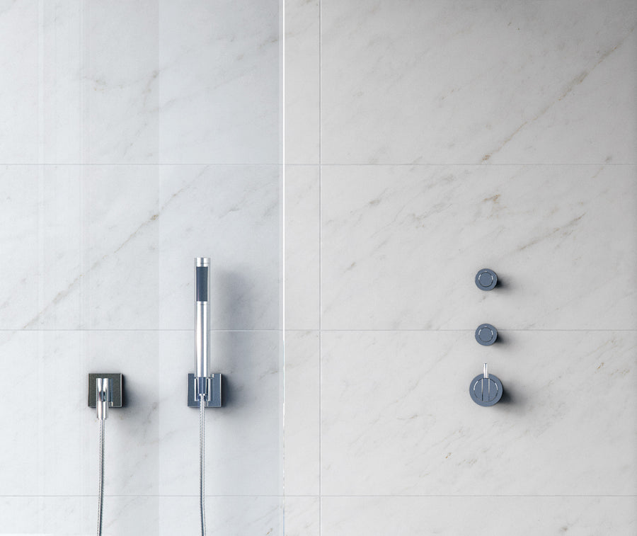 Minimalist shower setup with light gray marble tiles, a sleek silver handheld showerhead on the left, and three round silver knobs on the right for water control.