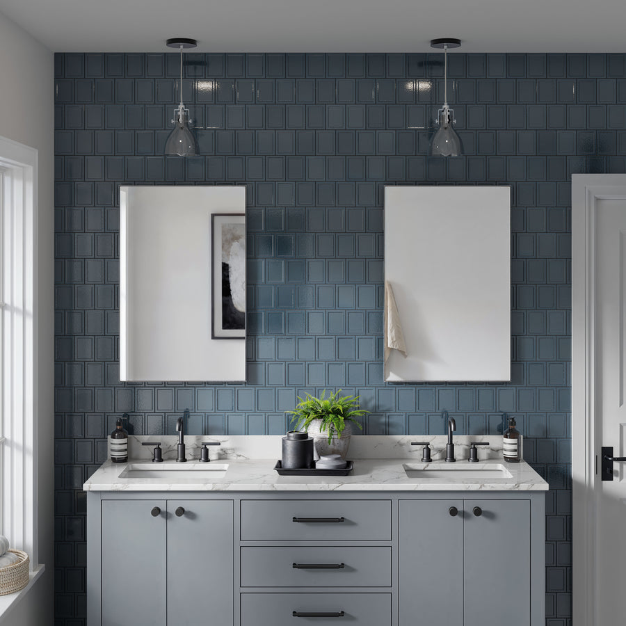A modern bathroom with a double sink vanity, marble countertop, blue square tiled backsplash, two rectangular mirrors, and glass pendant lights above each sink. A potted plant and soap dispensers are on the counter.