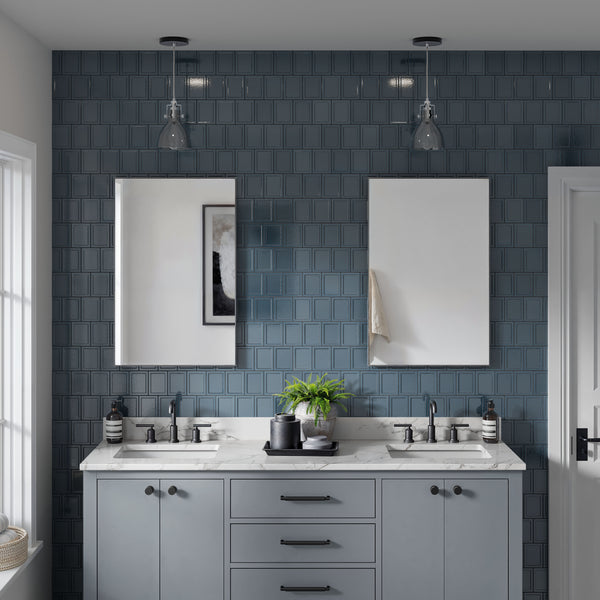 A modern bathroom with a double sink vanity, marble countertop, blue square tiled backsplash, two rectangular mirrors, and glass pendant lights above each sink. A potted plant and soap dispensers are on the counter.