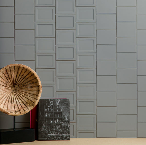 A decorative wooden gramophone and a black-and-white photo book are placed against a modern gray tiled wall with a geometric square pattern.