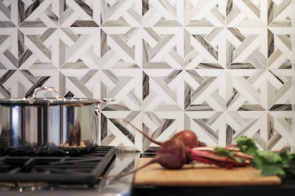 A kitchen scene with a geometric patterned tile backsplash, a stainless steel pot on a stove, and fresh beets with greens on a wooden cutting board in the foreground.