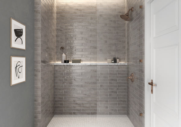 Modern walk-in shower with glossy gray subway tiles, two rainfall showerheads, built-in shelf holding toiletries, and minimalistic wall art glimpsed beside a white door. The space is sleek and well-lit.