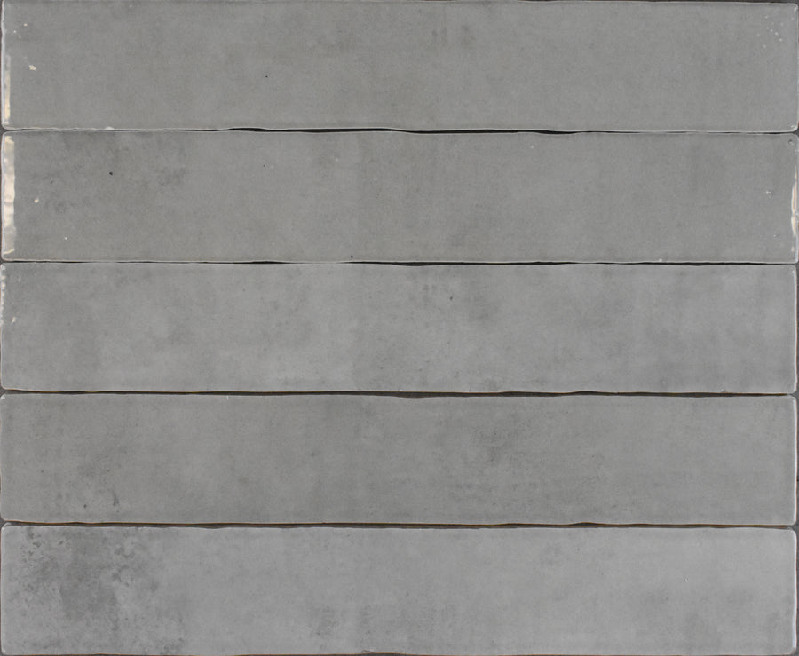 Six Marrakesh 2x16 Ceramic Tiles in grey are arranged horizontally, each featuring smooth, subtly varied tones and a textured surface for a minimalist, modern look.