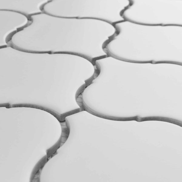 Close-up of white tiles with a Moroccan arabesque pattern, showing the raised, curved edges and the grout lines between each tile. The surface is smooth and glossy, giving a clean, modern appearance.