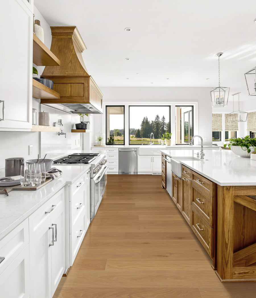 Bright, modern kitchen with white cabinets, wood accents, large island, stainless steel appliances, pendant lights, and big windows overlooking a scenic outdoor view. Green plants sit on the island countertop.