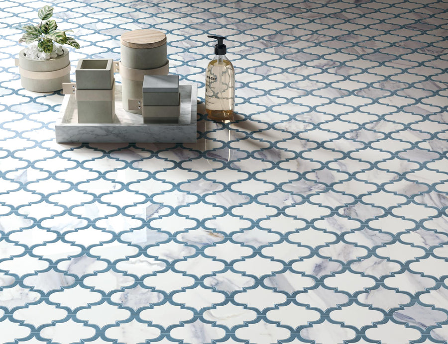 Decorative floor tiles with a white and blue geometric pattern. On the floor sits a marble tray holding boxes, a soap dispenser, and a small potted plant.
