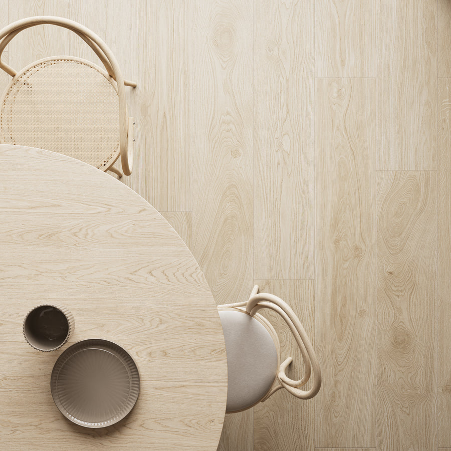 A top-down view of a light wooden table with two beige chairs. On the table are two plates and a bowl, all in neutral tones, creating a minimalist and modern dining setting. The floor is also light wood.