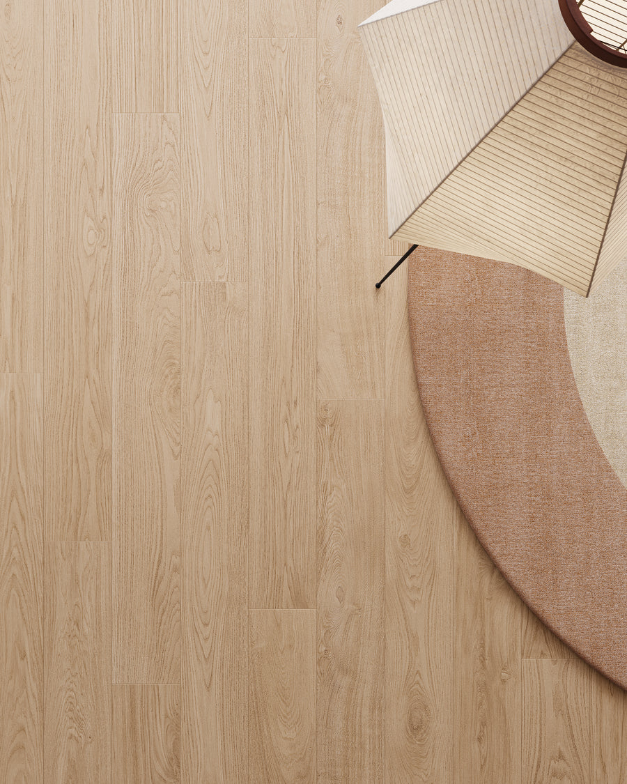 A round beige rug on light wood flooring, with part of a modern paper floor lamp and two folding paper fans arranged on the upper right corner of the rug. The overall style is minimalistic.