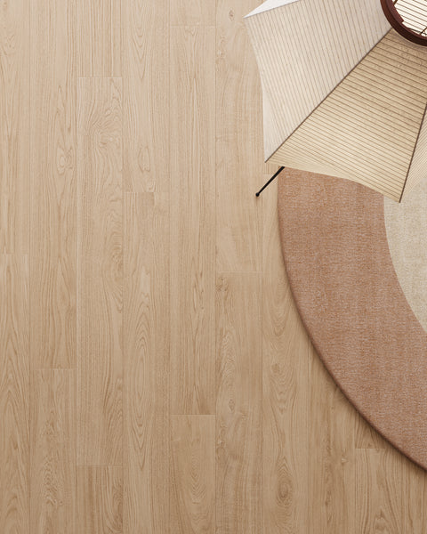 A round beige rug on light wood flooring, with part of a modern paper floor lamp and two folding paper fans arranged on the upper right corner of the rug. The overall style is minimalistic.