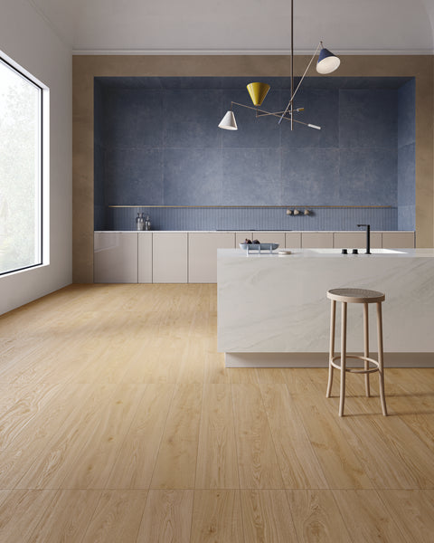 Modern kitchen with light wood flooring, a large marble island with a beige stool, minimalist white cabinets, blue tiled backsplash, and unique geometric pendant lighting. Large window brings in natural light.