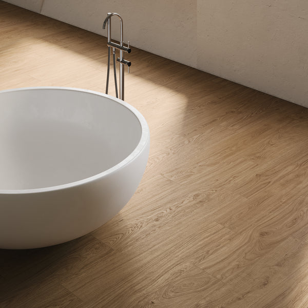 A modern white oval bathtub stands on a light wood-patterned floor in a minimalist room with soft natural light casting gentle shadows.