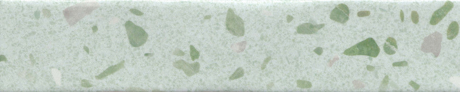 A close-up of the Fragmento 2x10 Ceramic Tile in Mint To Be shows a light green surface with scattered dark green and beige speckles, creating a bold terrazzo-inspired pattern reminiscent of decorative wall tiles.