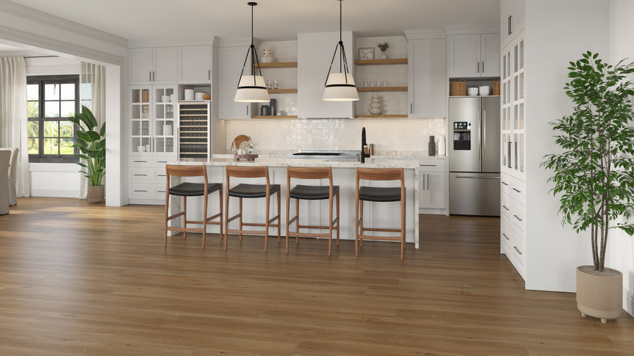 Modern kitchen with white cabinets, stainless steel appliances, an island with four wooden barstools, pendant lights, and wooden floors. There are plants and large windows letting in natural light.