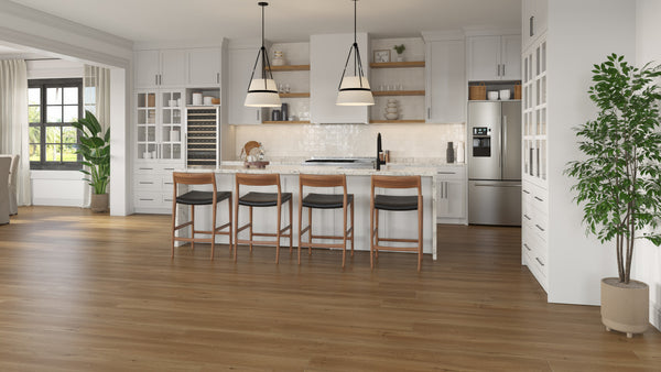 Modern kitchen with white cabinets, stainless steel appliances, an island with four wooden barstools, pendant lights, and wooden floors. There are plants and large windows letting in natural light.