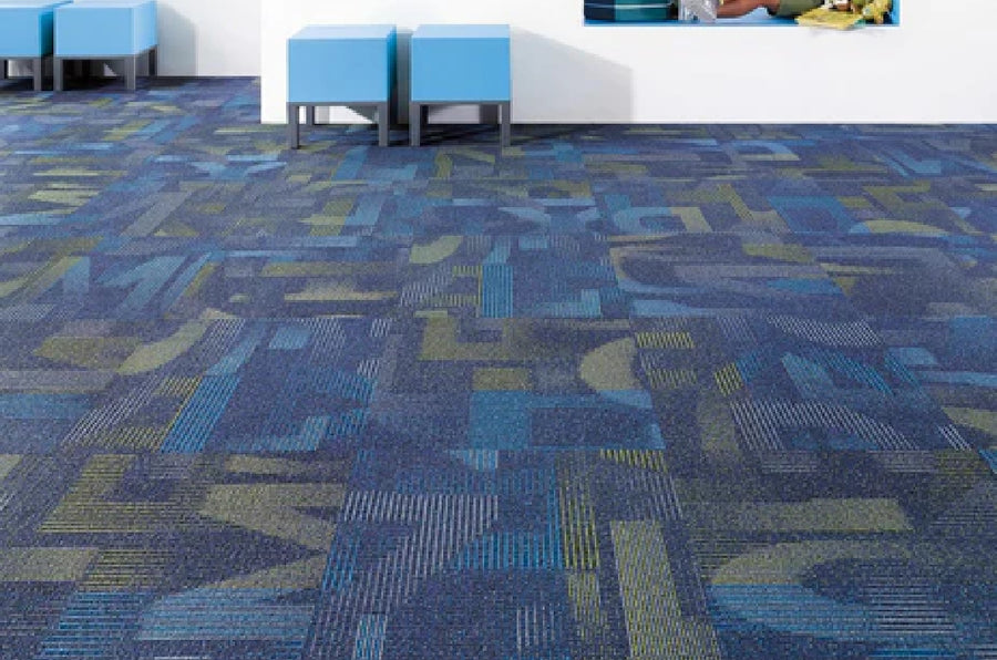 A vibrant commercial space featuring Commercial Modular Carpet Tiles in blue abstract letter shapes, complemented by blue ottomans and a white wall with a window seat with people sitting.