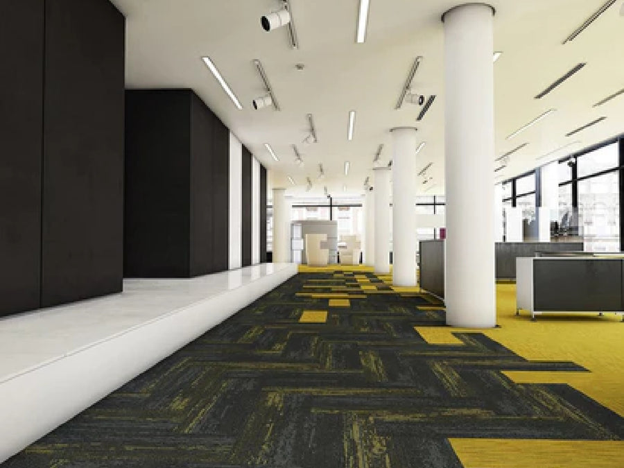 Modern office space featuring Commercial Modular Carpet Tiles in yellow and gray, with white columns, dark accent walls, large windows, defined work areas with desks and partitions, all brightly lit by ceiling lights.