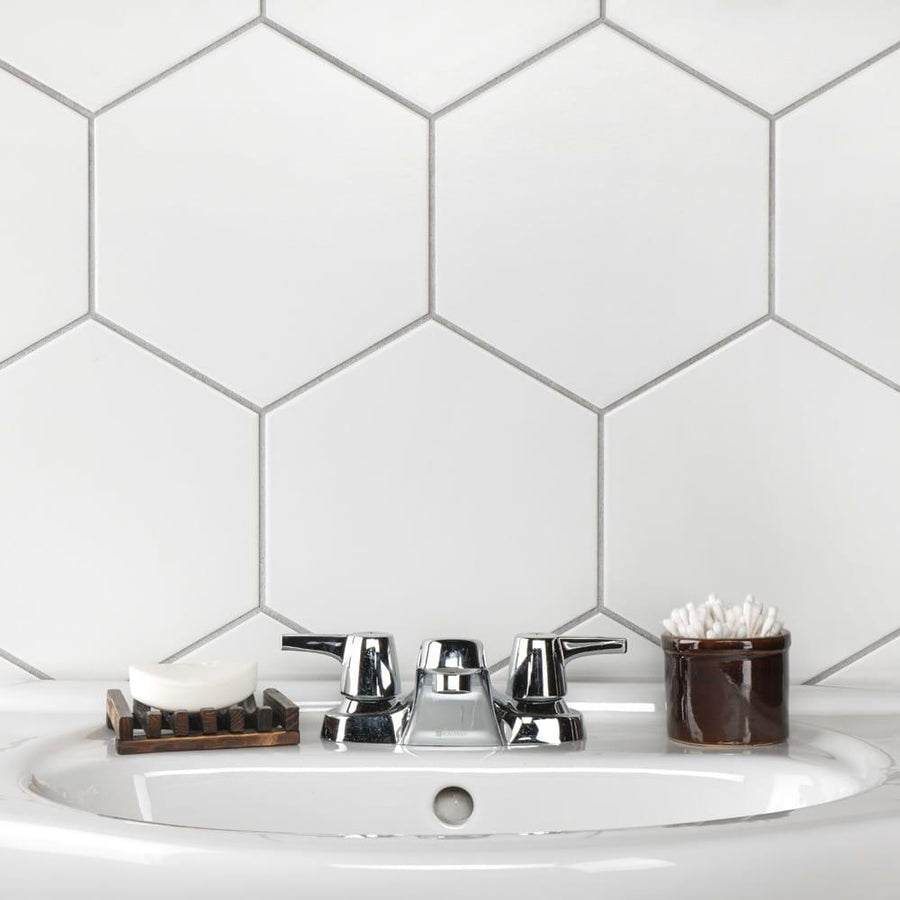A bathroom sink with a chrome faucet, a soap dish holding a bar of soap, and a brown container of cotton swabs, set against a white hexagonal tile backsplash.