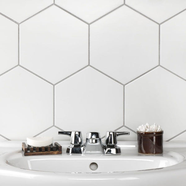 A bathroom sink with a chrome faucet, a soap dish holding a bar of soap, and a brown container of cotton swabs, set against a white hexagonal tile backsplash.