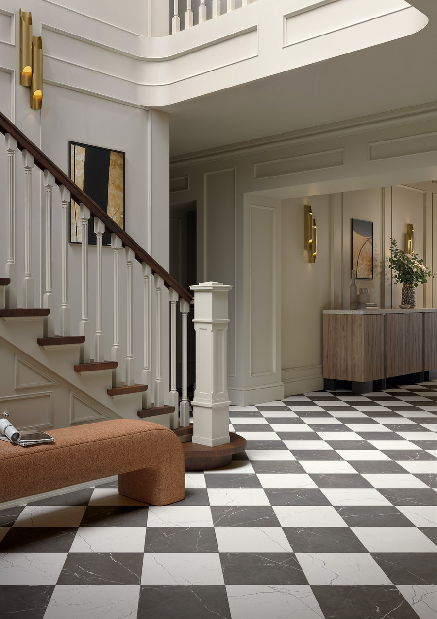 A bright foyer features Monaco 12x12 Glazed Porcelain Tile in black-and-white checkered pattern, a curved wooden staircase with white spindles, a rust bench, modern wall art, and a console table with a flower vase.