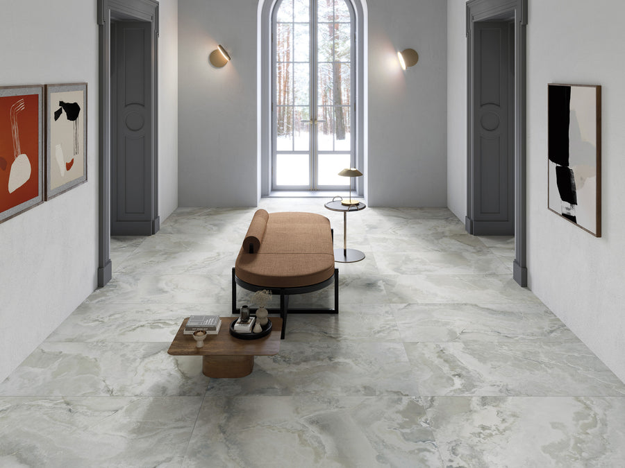 A modern hallway with marble flooring, a brown cushioned bench, a small coffee table, abstract wall art, grey doors, wall lights, and a large window showing a snowy landscape outside.