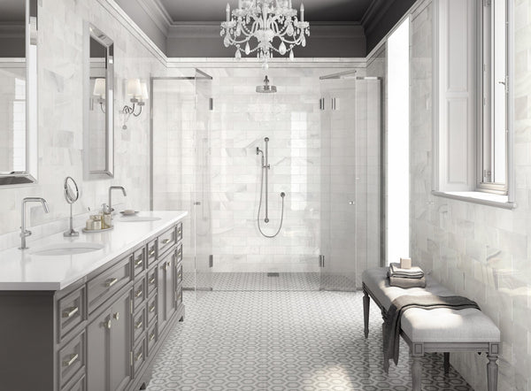 Elegant bathroom with double sinks, gray cabinets, large mirrors, chandelier, a walk-in glass shower, patterned tile floor, a cushioned bench, and a large window letting in natural light.