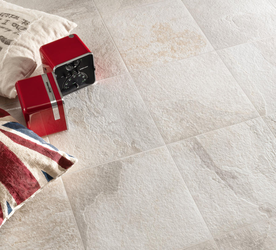 Beige textured floor tiles with a vintage red radio and two pillows, one with a Union Jack design and the other with faded text, placed on the floor.