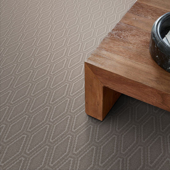 Close-up of a gray carpet with a subtle geometric pattern, next to the corner of a wooden table with a black dish on top.