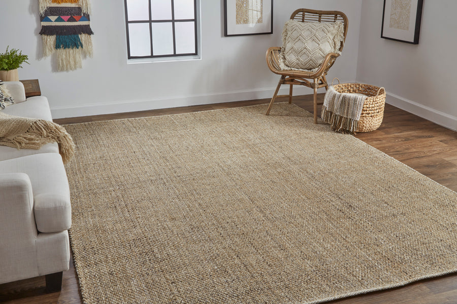 A cozy living room with a large beige woven rug on wooden floors, a white sofa with a blanket, a wicker chair with a cushion, a basket, and wall art beside a window letting in natural light.