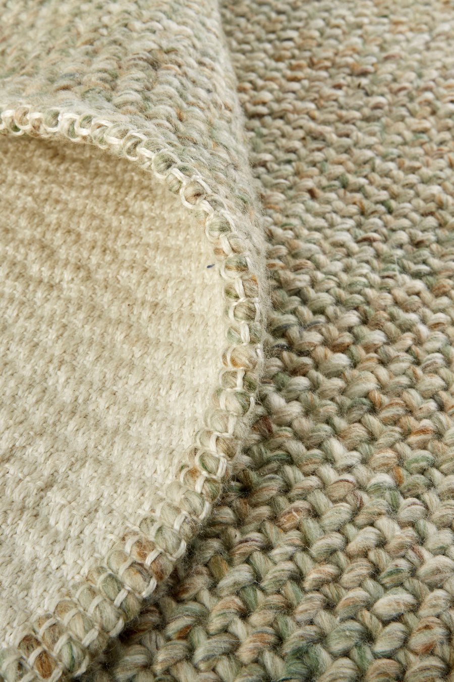 A close-up of a woven rug with natural beige, cream, and light green fibers, showing textured loops and the underside with visible stitching along the edge.
