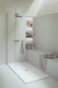 The NEOStone Point Center Drain Shower Base features a minimalist, modern white design with a low profile, glass partition, built-in bench draped with a towel, stacked towels, toiletries on recessed shelves, and soft natural light from above.