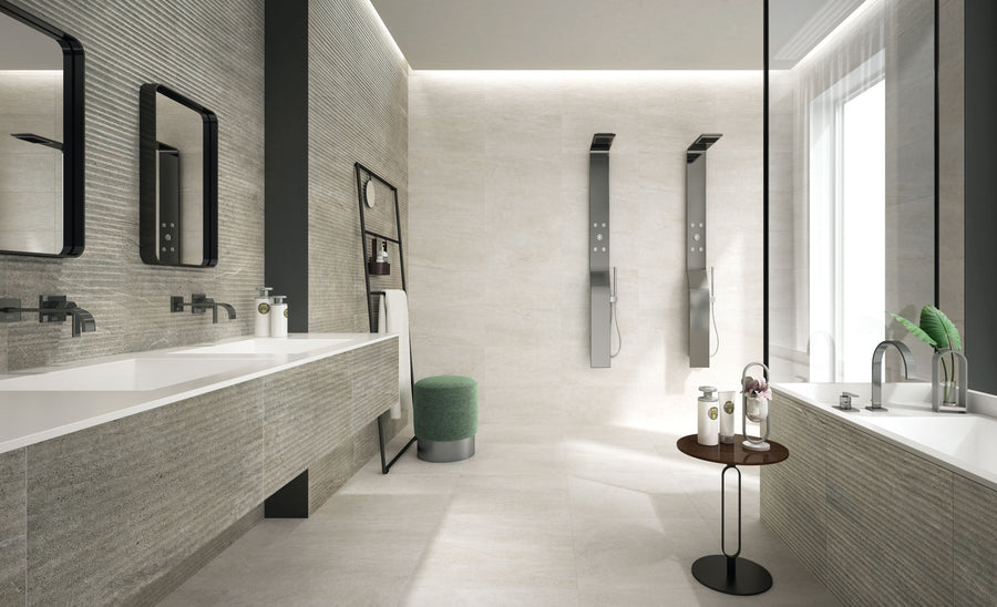 Modern bathroom with two wall-mounted sinks and mirrors on the left, two sleek shower panels on the back wall, a bathtub with a round side table and green plant on the right, and a green stool near the center.