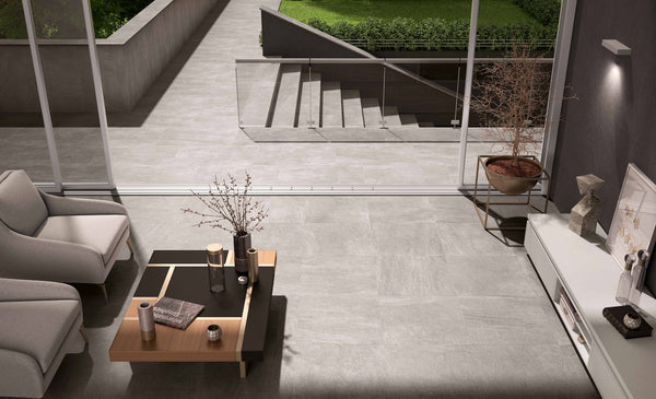 Modern living room with light gray tiled floors, a coffee table with decor, two armchairs, and a potted plant, next to large windows overlooking stairs and a green garden outside.