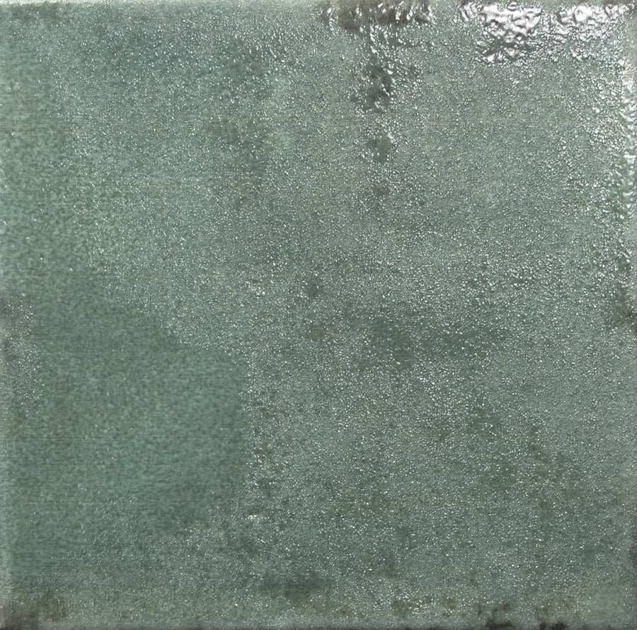 A close-up of the Nakama 5" x 5" Ceramic Tile in Green shows a square tile with a slightly glossy, uneven glazed surface. Subtle color and texture variations give it a handmade, rustic look.