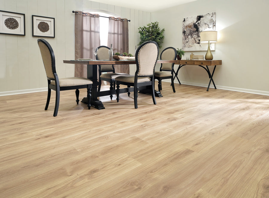 Bright dining room with light wood flooring, a dark wooden table with four upholstered chairs, a side desk with a lamp, abstract art, beige walls, and a window with brown curtains.