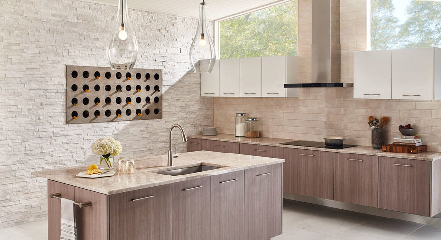 Modern kitchen with light wood cabinets, marble countertops, white tile backsplash, a central island with a sink, hanging pendant lights, wall-mounted wine rack, and large windows letting in natural light.