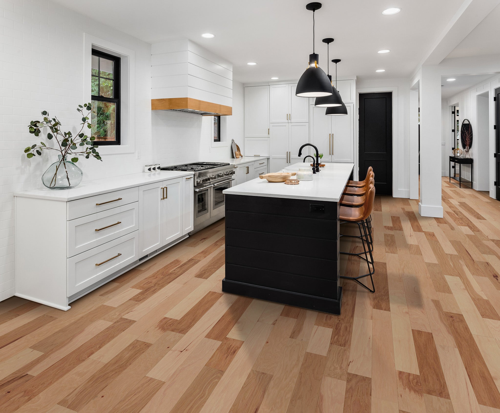 
		                            	Modern kitchen with white cabinets, wood accents, a black island with bar stools, pendant lights above, and stunning Deepwood Trail 5″ Hickory Oak Hardwood flooring. A vase with greenery sits on the countertop by the window.
		                            