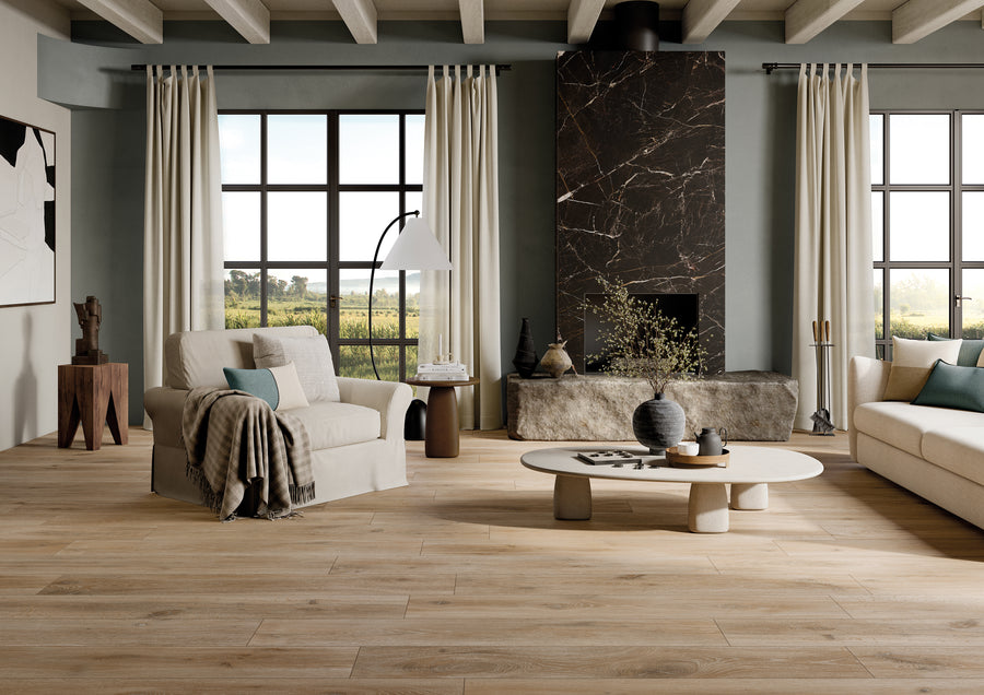 A modern living room with large windows, light-colored sofas, a round coffee table, a tall floor lamp, neutral decor, wood-look flooring, and a dark marble fireplace. Natural light fills the stylish, cozy space.